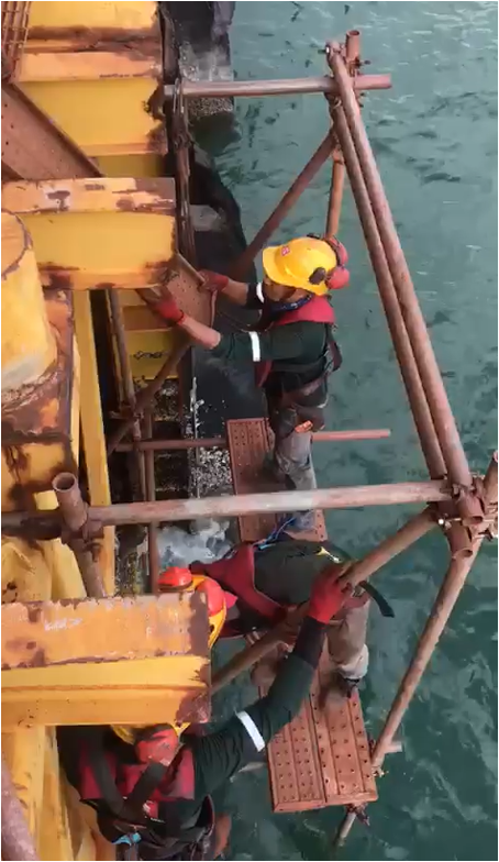 Three men working on a suspended scaffold over the sea, using tubular heavy-duty materials for a project with Vale Malaysia Mineral Sdn Bhd